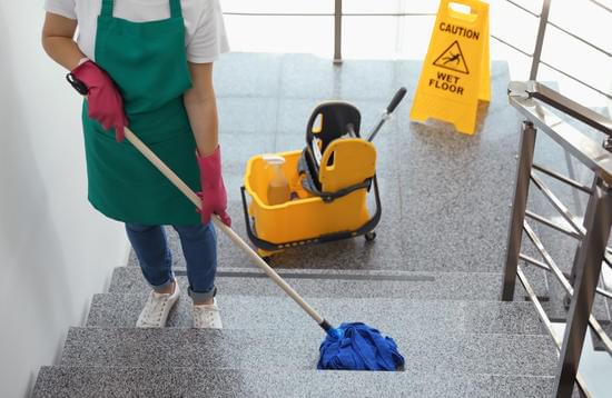 Trabajadora limpiando con una fregona los escalones de una escalera